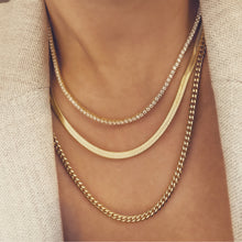 Load image into Gallery viewer, woman in a beige blazer wearing sanza jewelry Vienna necklace set which is a three layered necklace. The tennis cubic zirconia necklace sits first at 16 inches then the herringbone necklace sits at 18 inches and last the cuban link chain necklace sits at 20 inches in length. All three necklaces are 14 karat gold filled.   
